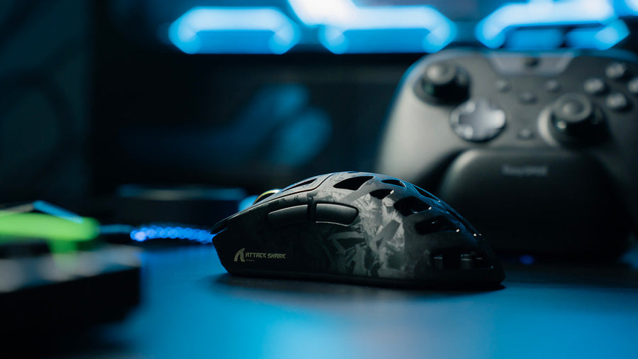 Black ATTACK SHARK lightweight gaming mouse on a blue-lit gaming desk with controller in background